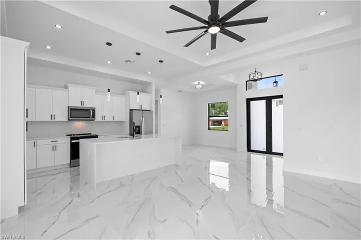 Kitchen with stainless steel appliances, an island with sink, open floor plan, white cabinets, and a raised ceiling