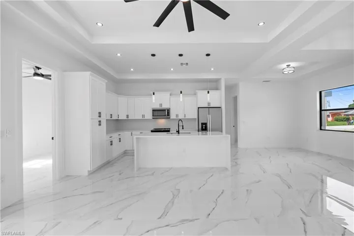 Kitchen with ceiling fan, a center island with sink, stainless steel appliances, pendant lighting, and white cabinets