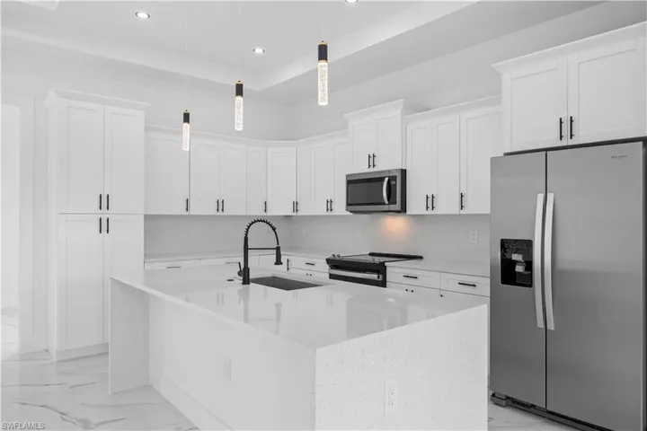 Kitchen with stainless steel appliances, light stone countertops, a tray ceiling, white cabinetry, and tasteful backsplash