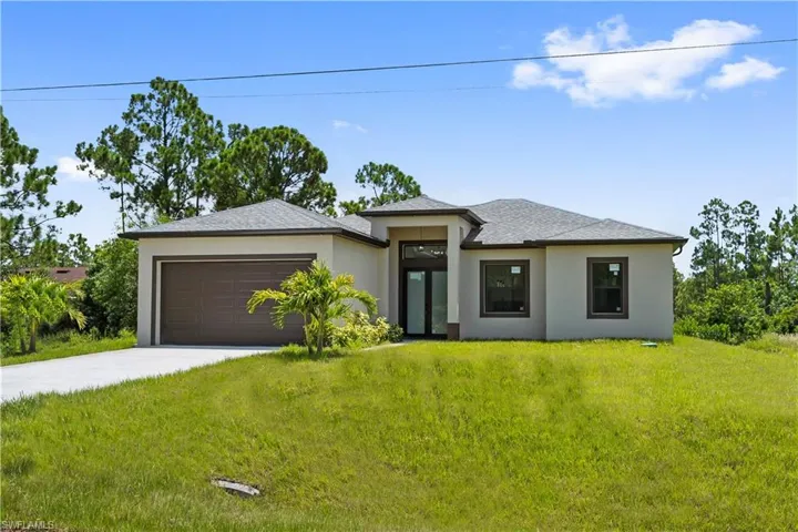 Prairie-style house featuring a front yard, driveway, stucco siding, an attached garage, and a shingled roof