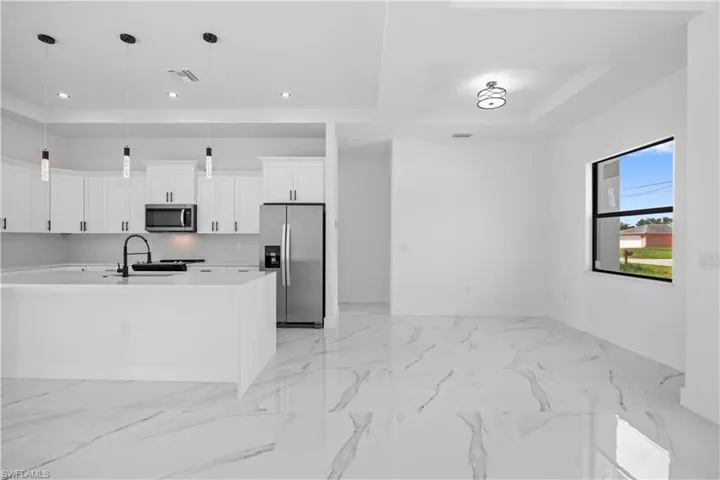 Kitchen with stainless steel appliances, white cabinetry, light stone counters, decorative light fixtures, and a center island with sink
