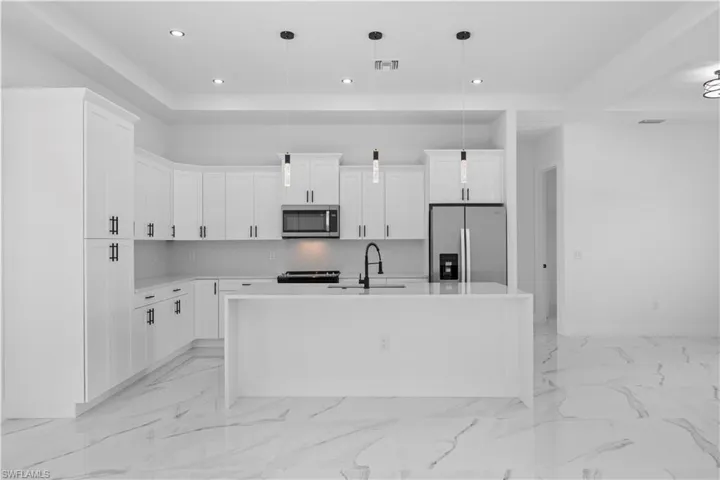 Kitchen with a center island with sink, stainless steel appliances, light stone counters, white cabinetry, and pendant lighting