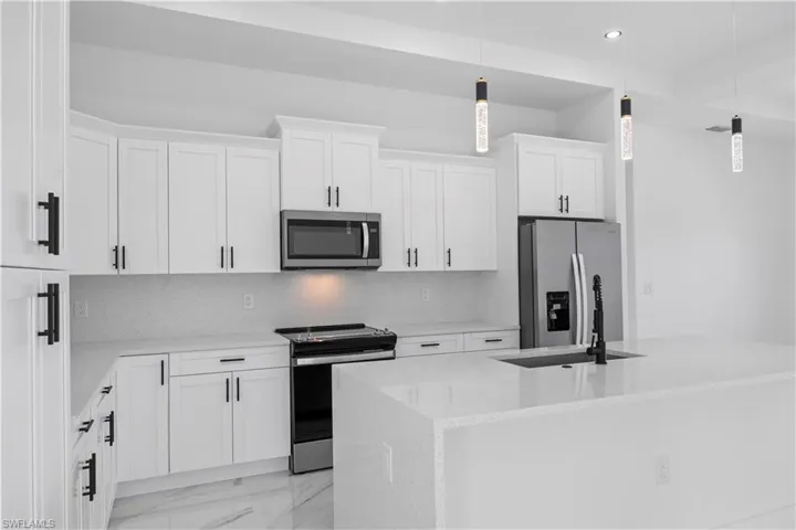 Kitchen featuring stainless steel appliances, light stone counters, white cabinetry, a center island with sink, and light marble finish floors