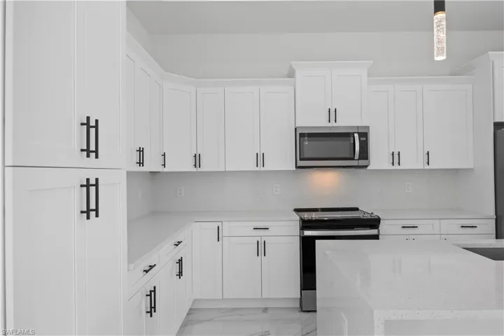 Kitchen with stainless steel appliances, backsplash, white cabinets, light stone counters, and light marble finish flooring