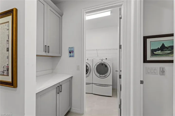 Garage entry with STAGGERED TILE FLOOR, pantry, “DROP ZONE” with cabinetry and solid surface countertop, and laundry room with TILE FLOOR, washer, and dryer.