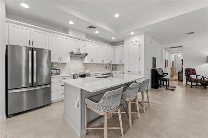 Open kitchen with EXTERNALLY VENTED HOOD RANGE, upgraded cabinetry with crown molding, STAGGERED TILE FLOOR, QUARTZ COUNTER, tile backsplash, one bowl stainless steel under mount sink, stainless steel appliances, self-cleaning glass smooth top CONVECTION RANGE OVEN, garbage disposal, and island with breakfast bar, one bowl sink and UPGRADED FAUCET with sprayer and pantry.