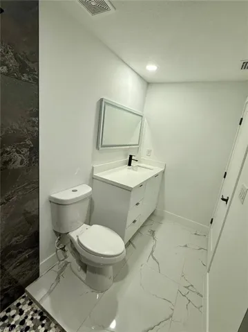 Bathroom with baseboards, visible vents, toilet, marble finish floor, and vanity