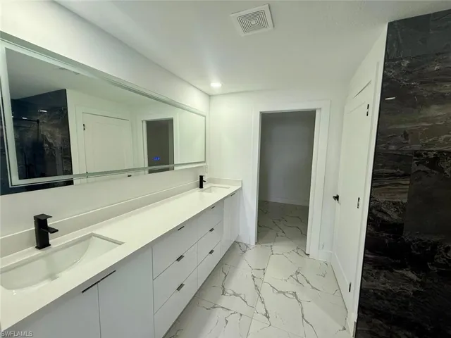 Full bath featuring double vanity, marble finish floor, visible vents, and a sink