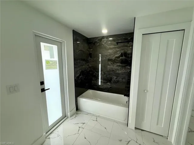 Bathroom featuring a closet, marble finish floor, a bathtub, walk in shower, and a wealth of natural light