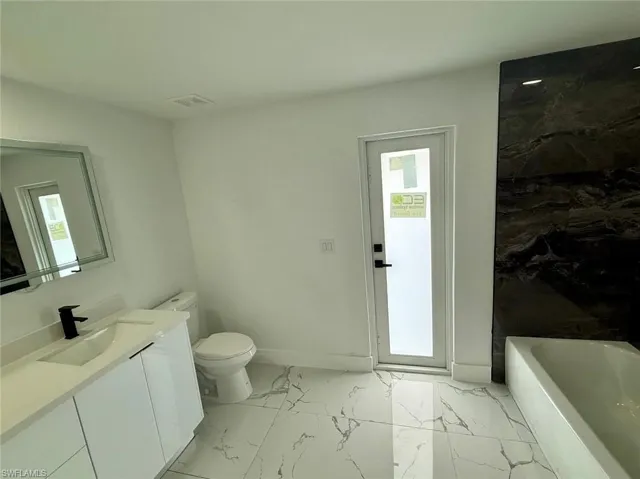 Bathroom with a washtub, marble finish floor, toilet, a healthy amount of sunlight, and vanity