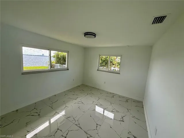 Spare room with marble finish floor, a water view, visible vents, and baseboards