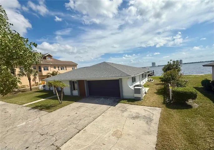 View of front of house featuring driveway, a shingled roof, a water view, an attached garage, and a front yard