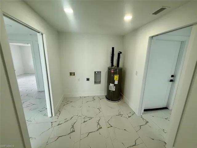 Utility room featuring electric panel, visible vents, and electric water heater