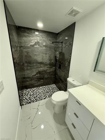 Full bathroom with toilet, vanity, visible vents, marble finish floor, and a marble finish shower