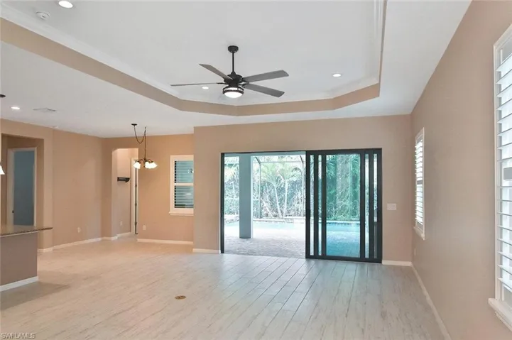 Large tiled Great Room with tray ceiling and triple sliders leading to the Lanai, pool, and outdoor Kitchen