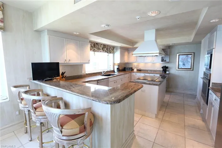 Kitchen featuring a peninsula, island range hood, white cabinetry, a kitchen island, and a kitchen bar