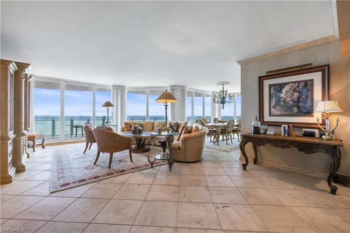 Living room with expansive windows, a water view, suspended lighting, and stone tile flooring