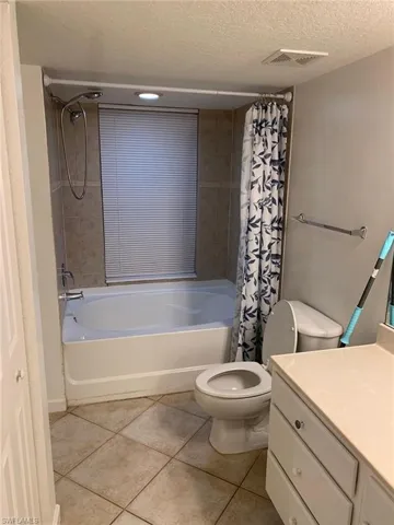 Full bathroom featuring toilet, a textured ceiling, shower / bath combo with shower curtain, and tile patterned flooring