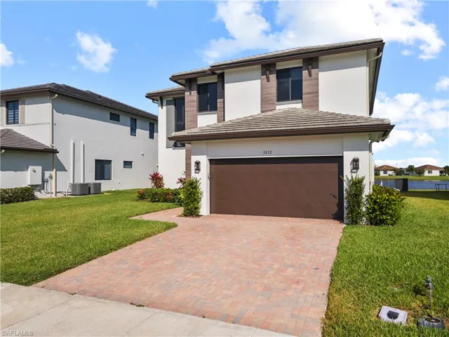 View of front of home featuring a tile roof, stucco siding, a yard, and decorative driveway