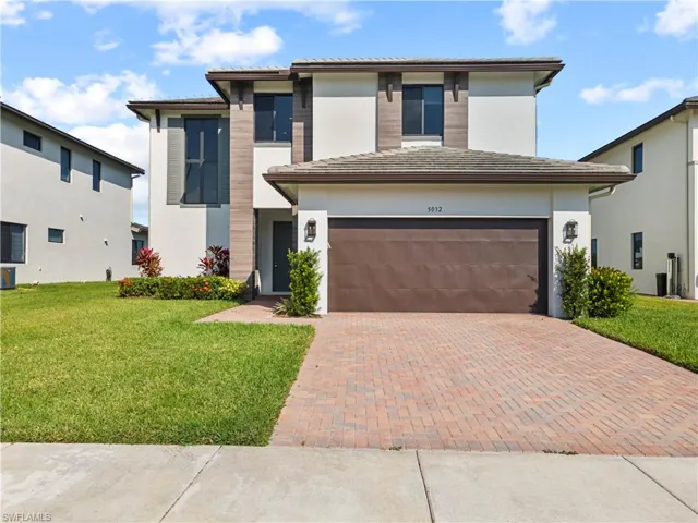 View of front of home featuring a tile roof, stucco siding, a yard, and decorative driveway