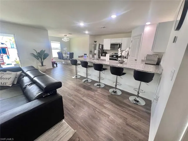 Kitchen with a kitchen bar, a peninsula, stainless steel appliances, dark wood-type flooring, and light stone counters