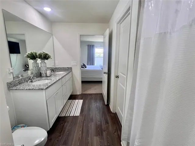 Ensuite bathroom featuring double vanity, dark wood-type flooring, and a shower with shower curtain