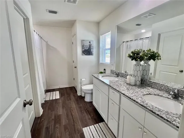 Full bath featuring double vanity, dark wood-type flooring, and a shower with shower curtain