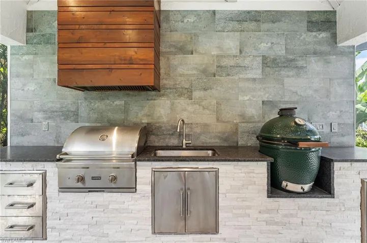 The outdoor cabana features a Coyote grill and Big Green Egg, complemented by a striking blue porcelain backsplash, a stacked stone accent wall, and a beautifully appointed pool bath.