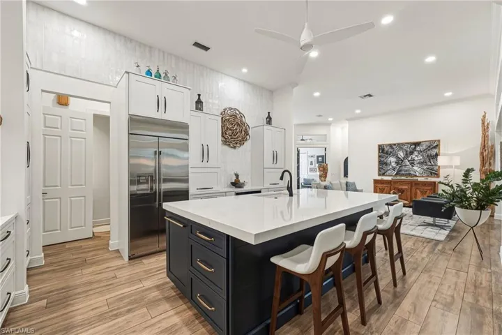 The reimagined kitchen showcases an expansive quartz island, bespoke custom cabinetry, premium stainless steel appliances, and a striking vertical tile backsplash, all illuminated by recessed lighting and seamlessly open to the living areas—ideal for both grand entertaining and intimate gatherings.