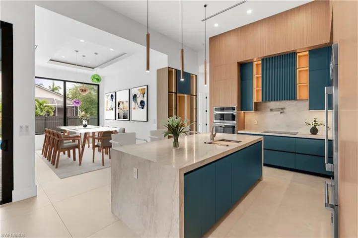 Kitchen featuring modern cabinets, light stone countertops, pendant lighting, an island with sink, and recessed lighting
