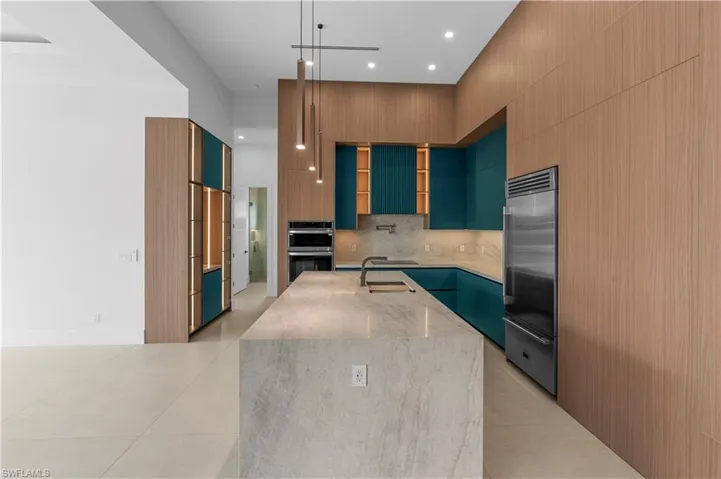 Kitchen with modern cabinets, hanging light fixtures, light stone counters, stainless steel appliances, and light tile patterned floors