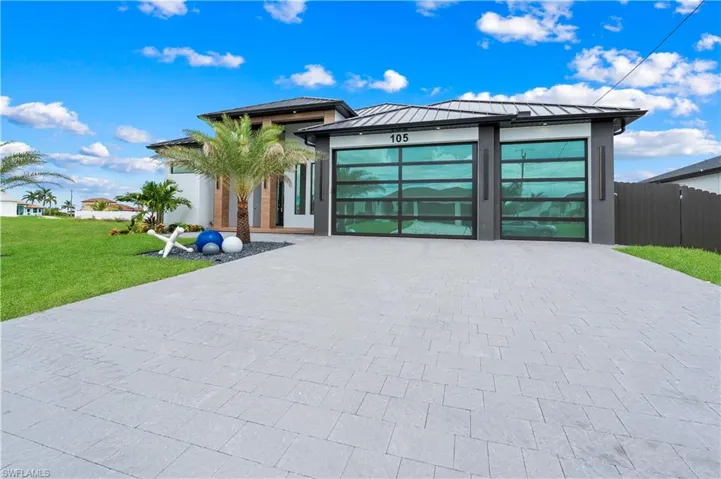 View of front facade with decorative driveway, a standing seam roof, a metal roof, an attached garage, and stucco siding