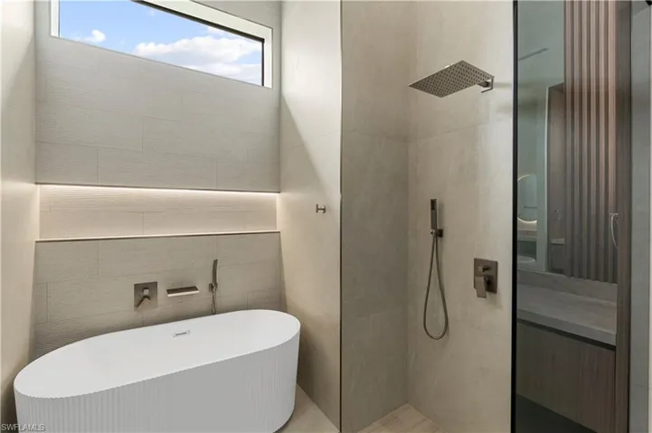 Bathroom with a freestanding tub, walk in shower, tile walls, and vanity
