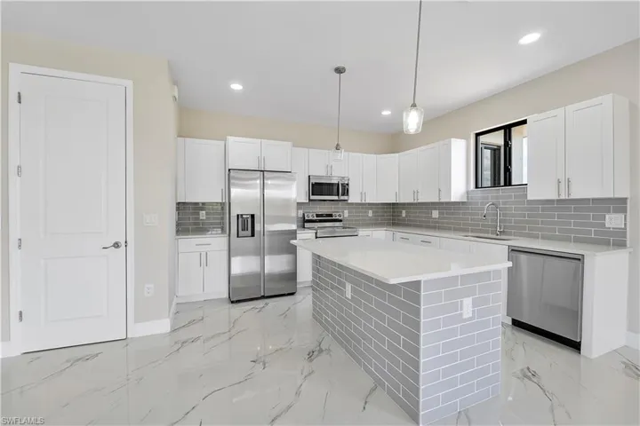 Kitchen featuring stainless steel appliances, a center island, tasteful backsplash, light stone counters, and white cabinetry