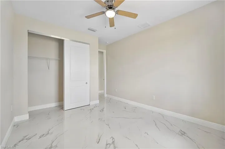 Unfurnished bedroom with light marble finish floors, a ceiling fan, and a closet