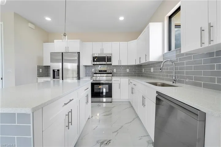 Kitchen featuring stainless steel appliances, light stone countertops, a kitchen island, and light marble finish flooring