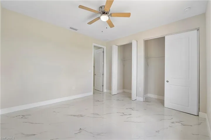 Unfurnished bedroom featuring two closets, ceiling fan, and light marble finish flooring