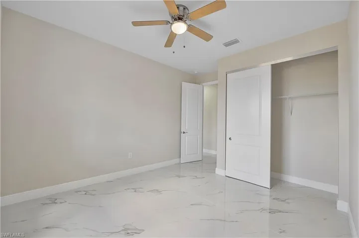 Unfurnished bedroom featuring ceiling fan, a closet, and light marble finish floors