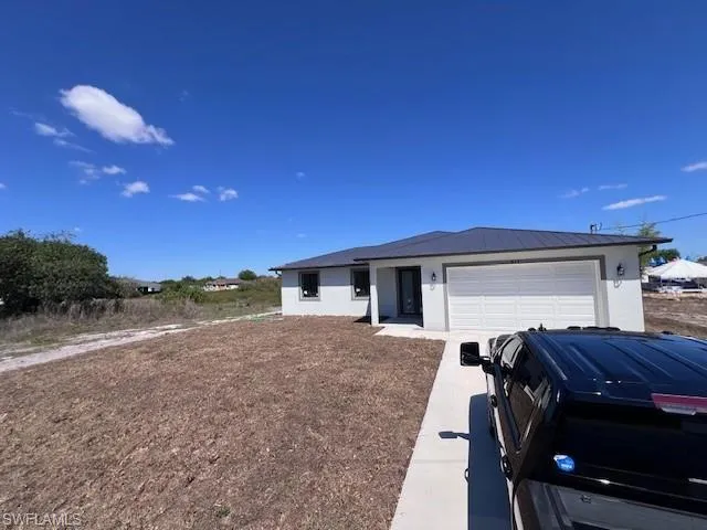 Single story home featuring stucco siding, a garage, concrete driveway, and a metal roof