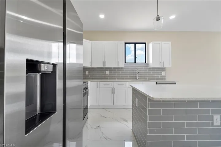Kitchen with stainless steel refrigerator with ice dispenser, white cabinetry, backsplash, and light stone countertops