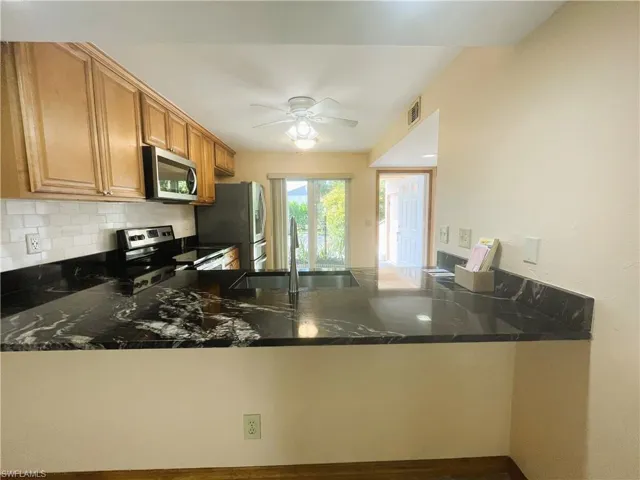Kitchen featuring stainless steel appliances, backsplash, a peninsula, dark stone countertops, and ceiling fan