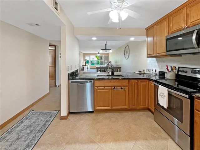 Kitchen with stainless steel appliances, dark stone counters, brown cabinetry, light tile patterned floors, and a peninsula