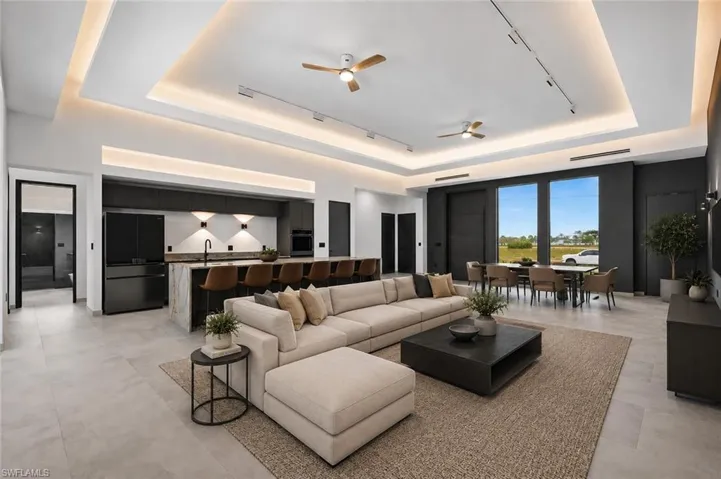 Open-concept living space with light-toned flooring, tray ceilings with accent lighting, and recessed light fixtures