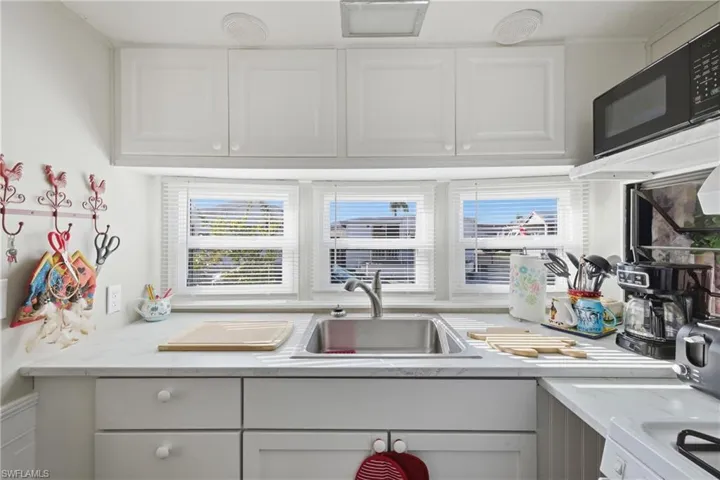 Kitchen with white cabinetry, black microwave, white stove, and light stone counters