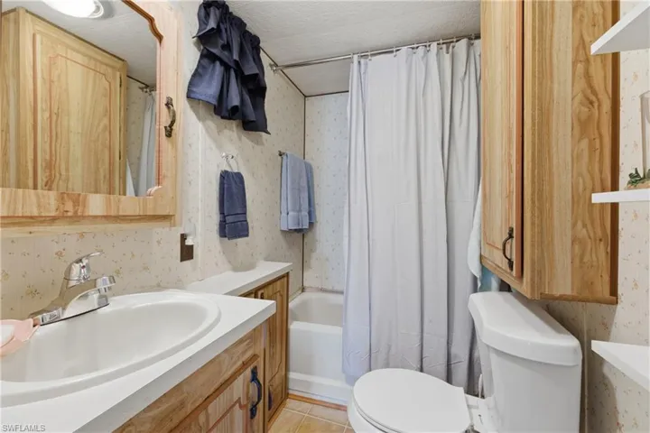 Bathroom with wallpapered walls, vanity, shower / bathtub combination with curtain, and a textured ceiling