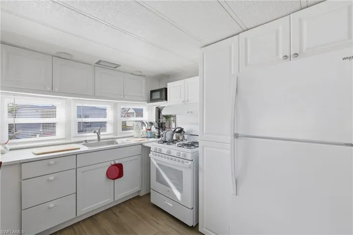 Kitchen featuring white appliances, white cabinets, dark wood finished floors, light countertops, and under cabinet range hood