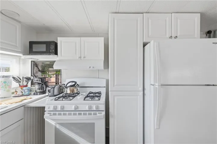 Kitchen with white appliances, white cabinetry, light countertops, and under cabinet range hood