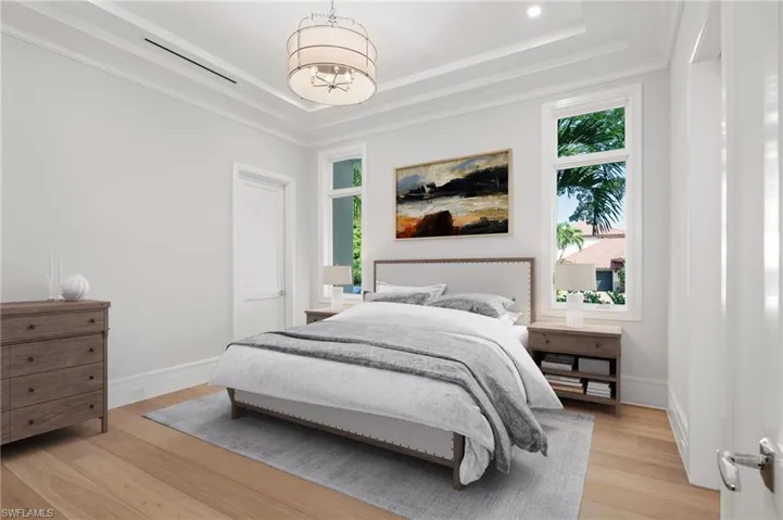 Bedroom with a tray ceiling, a notable chandelier, and light hardwood / wood-style flooring