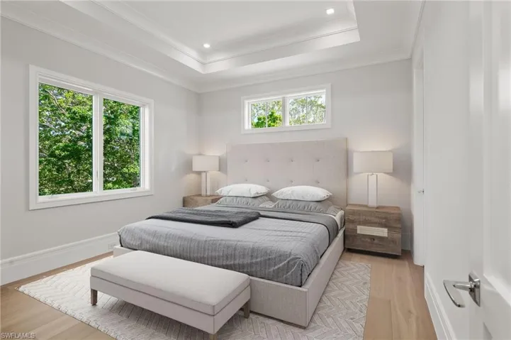 Bedroom with wood-type flooring, a tray ceiling, crown molding, and multiple windows
