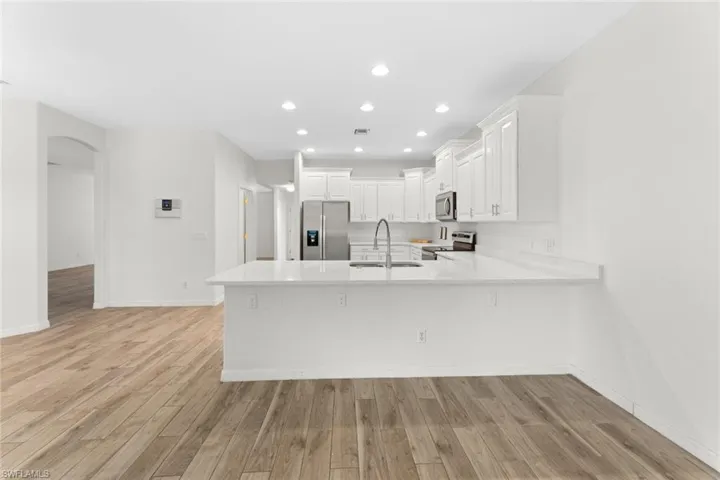 Kitchen with appliances with stainless steel finishes, white cabinetry, sink, and light hardwood / wood-style flooring